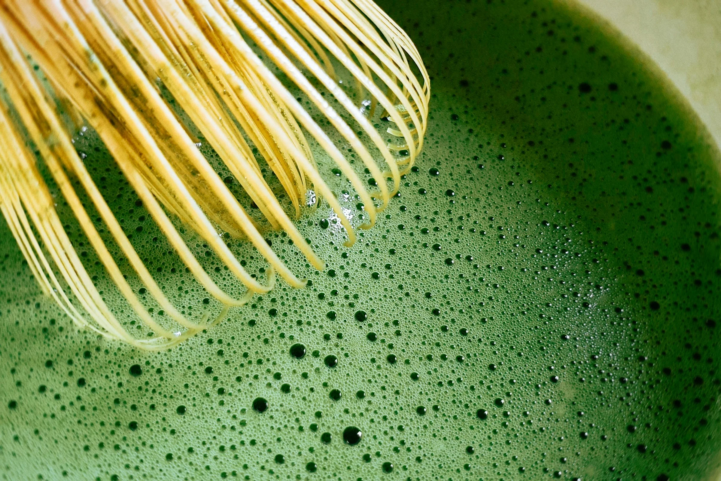 Bamboo whisk raising a fine green foam on freshly whisked matcha